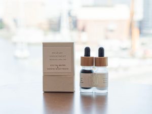 明るい日差しの窓辺に、二色のインク瓶（キャップがスポイト式）、風合いのある質感の紙箱が並ぶ。窓の外には桜木町の海際がぼんやりと見える。