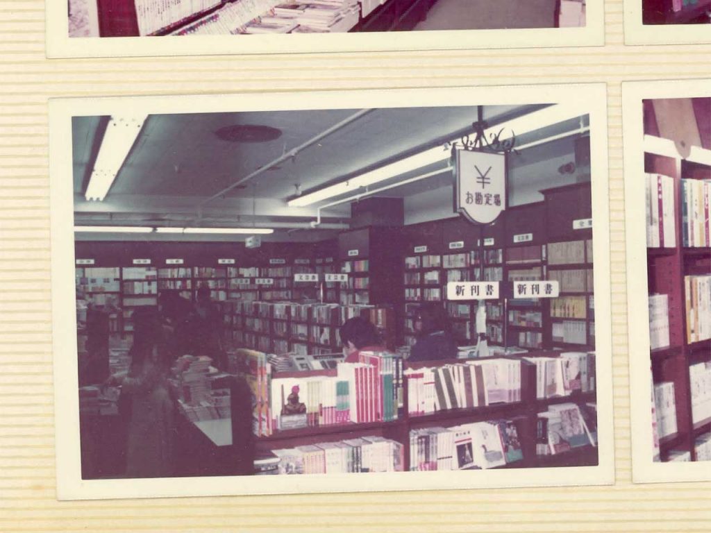 アルバムに貼られた紙写真。書棚が並ぶ店内、天井から「お勘定場」の看板が下がっている