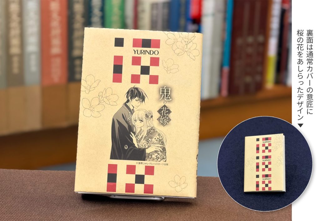 特典ブックカバーを本につけた状態の見本。有隣堂ブックカバーの色違いで、中央に人物イラスト、周囲に桜の花