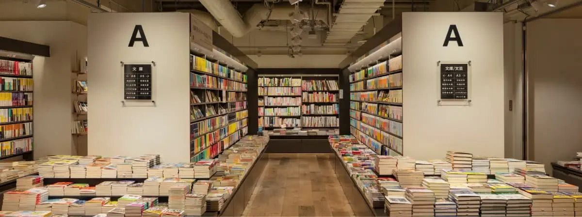 背の高い書棚が両側と奥の壁面に並ぶ、書店の売場イメージ