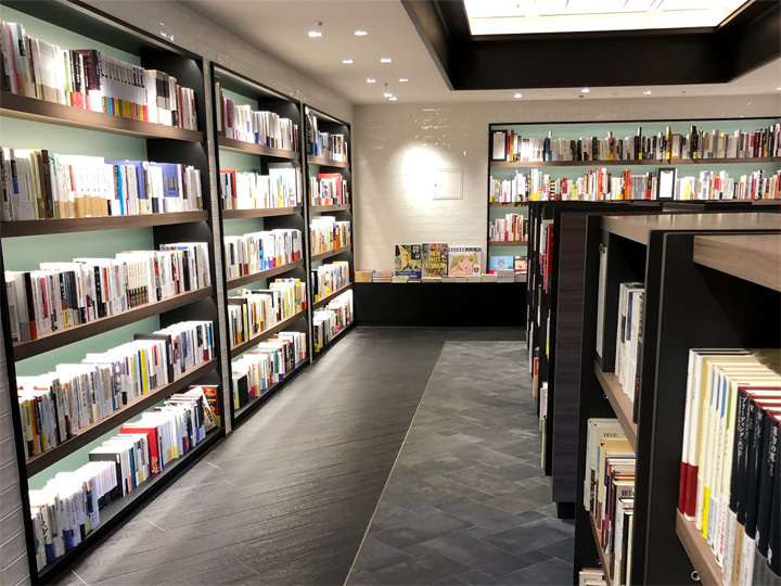BACONのブックエリア（カフェに併設された書店／書籍売場）。落ち着いた色合いのスペース、壁面と中央に書棚が並んでいる。