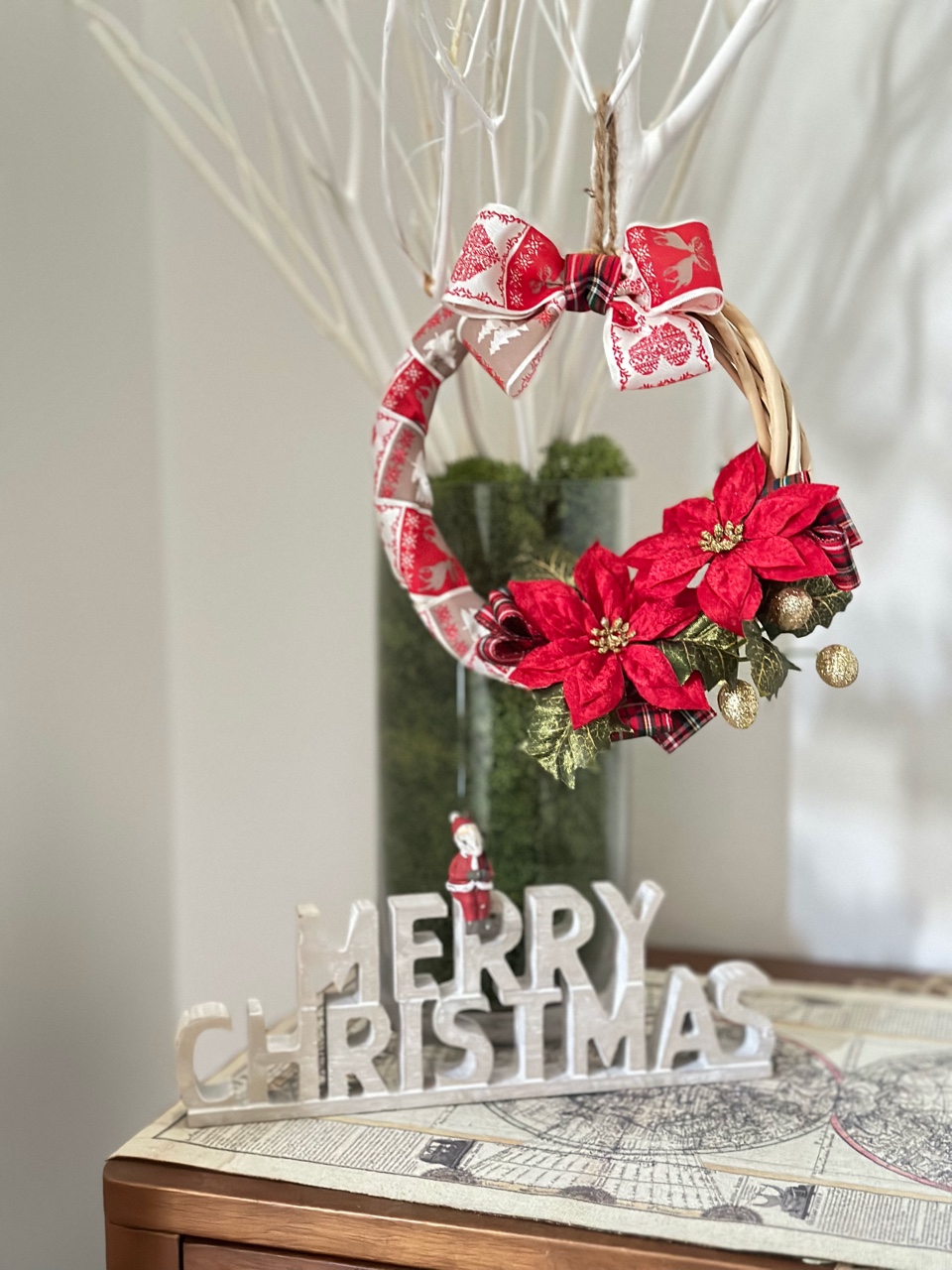 ポインセチアを使用したクリスマスリース。台の上の花瓶に生けた白い枝にリースをかけた、クリスマスディスプレイのイメージ。