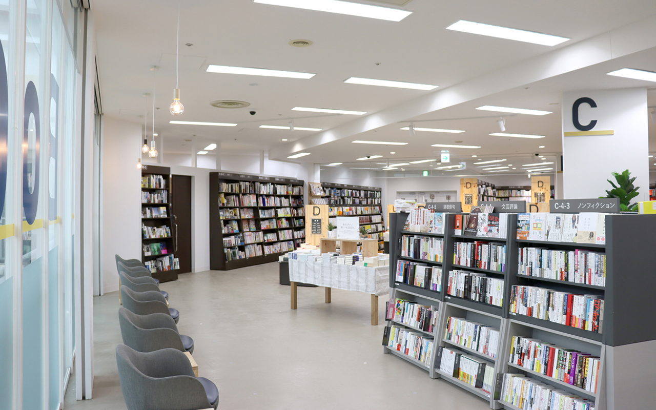 日差しが入るガラスの壁面に沿って1人掛けソファが並び、正面に背の低い文芸書の書棚