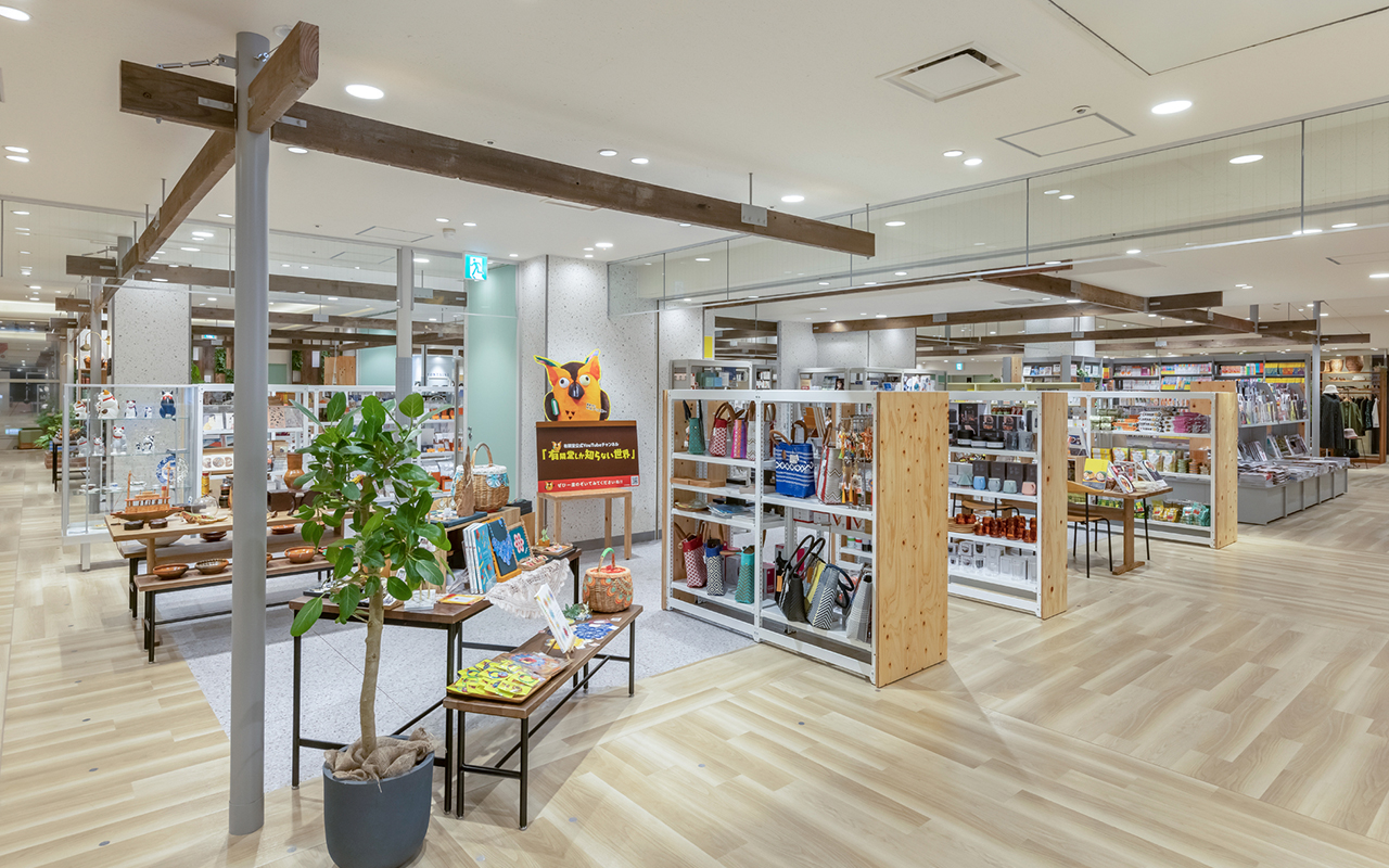 館内通路からみた店舗、雑貨ゾーン側。明るい色のテーブルと背の低い棚に商品がディスプレイされている。