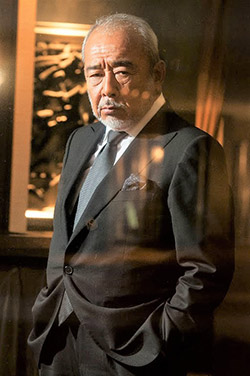 北方謙三の人物写真、シングルスーツを着てガラス越しにこちらを見ている